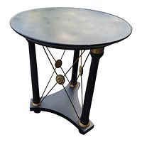 Front angled view of black round table with three column legs and gold gilt brass decorative accents.