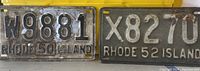 Close-up photo of two Rhode Island license plates side by side, one dated 1950, the other 1952, showing embossed characters with signs of rust and wear.