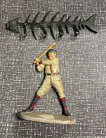 Cast iron fish skeleton wall hanger and baseball player door stopper figurine shown from the front on a textured surface.