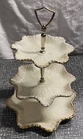 Front view of three-tiered ceramic dessert tray showing scalloped, petal-shaped plates with gold trim and metal posts with gold handle