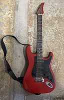 Full body of red electric guitar with strap laying on a carpeted floor