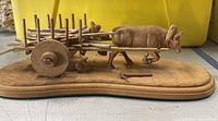 Side view of the hand-carved wooden ox cart sculpture showing detailed ox figure and wooden cart mounted on oval base.