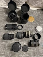 Six camera lenses laid out with lens caps and cases on a cloth surface.
