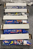 Lot of five NASCAR diecast semi trucks, all in original white boxes, stacked on floor.