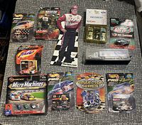 Photo showing variety of NASCAR die-cast cars, cardboard autograph cutout, collectible truck, and sets on a gray surface.