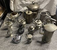 Full display of the 13-piece vintage pewter set showing various functional and decorative tableware items.