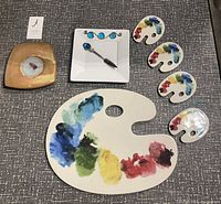 Full set of ceramic serving pieces including artist palette dishes, a square plate, and a spoon on a white plate.