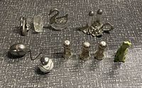 Image showing various salt and pepper shakers arranged on a gray surface including metal, glass, and ceramic pieces.