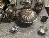 Front view of the entire silverplate collection including teapots, serving dish, creamer, and bowl on a textured surface.