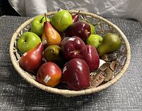 Top view of basket filled with realistic artificial fruit replicas including apples and pears in different colors, showing labels and naturalistic look.
