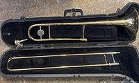 Photo showing full trombone including the bell section and slide placed in a fitted black hard case with interior lined in black fabric.