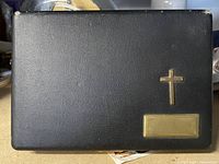 Closed black textured leather case with a gold cross and blank plate on the lid.