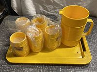 Yellow Rubbermaid picnic set arranged on a surface including a pitcher, tray, and eight tumblers wrapped in plastic.