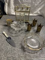 Full view of vintage barware and decor pieces including decanters, shot glasses, bowls, serving utensil, and clock arranged on fabric