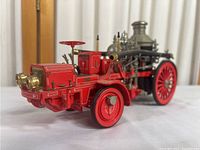 Front-side angle showing detailed red body with gold accents, headlights, and large red wheels with brass fittings.