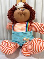 Full view of Cabbage Patch Koosas doll showing face, striped body, and rainbow suspenders.
