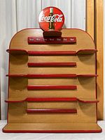 Full view of wooden perpetual calendar stand with red horizontal bars and circular Coca-Cola logo sign