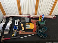 Photo of assorted tools on black cloth including pipe wrench, vises, clamps, staple gun, adjustable wrench, drill bits, two cans of thread sealant, and boxed soap dispensers.