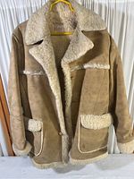 Front view of the tan vinyl suede jacket with large shearling collar and trim on pockets and cuffs. Hanging on yellow hanger.