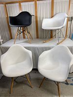 Photo showing one black modern rocker chair and one white rocker chair elevated on a platform, with two white modern armchairs placed below.