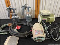 Full view of the paint spraying collection including two metal spray guns, hoses, a Mark II sprayer motor, and a Spravito compressor.