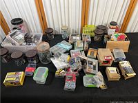 Overview of assorted hardware items including jars, boxes, and plastic containers with screws and nails on a black surface