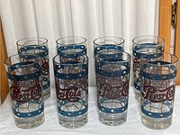 Set of eight tall vintage Pepsi Cola glasses arranged in two rows, showing the red logo and blue geometric pattern.