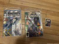 Photo of two Punisher first edition comics and one Marvel collectible card laid on a surface, comics in plastic sleeves.