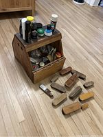 Full view of the shoe shine kit showing wooden box, shoe polish tins on top, and multiple wooden brushes placed around it