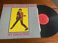 Vinyl LP album My Aim Is True by Elvis Costello, with the record partially removed from the cover, showing red label.