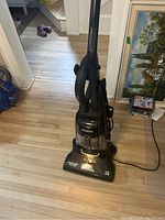 Full view of the upright black Eureka vacuum cleaner with clear dust container, standing on hardwood floor.