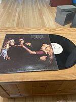 Front cover of Fleetwood Mac Mirage vinyl record showing three band members in a dark background and the record partially out of sleeve.