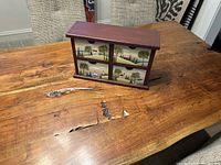 Front view showing the small painted chest with four drawers closed, placed on a natural wood table.