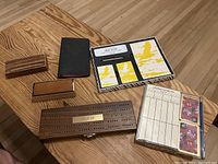 Overview of all items on a wooden table, showing wooden dominoes box, cribbage board, score pad, card decks, and small wooden boxes.
