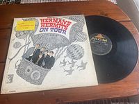 Front cover of the Herman's Hermits On Tour vinyl album showing illustrated hot air balloon with band members and a yellow promotional sticker.