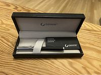 Open black box displaying the silver and black Messmer pen along with a guarantee booklet inside.