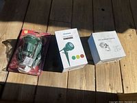 Photo of three boxed LED landscape spotlights and one green floodlight holder in packaging on wooden floor.