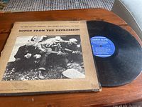 Front cover of the vinyl record sleeve titled 'Songs From The Depression' showing a black-and-white image of men playing guitar and other instruments.
