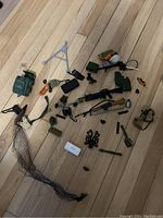 Top-down shot of full assortment of GI Joe military accessories scattered on wood floor, showing variety and condition.