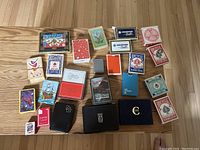 Top-down photo showing an assortment of 23 vintage and travel playing card decks and some cases on a wooden floor.
