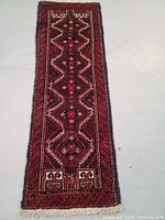 Full view of the narrow hand knotted Balouch wool rug showing its typical red and black geometric design with hints of blue and white.