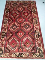 Full view of rug on floor showing geometric medallion pattern in red, black and ivory.