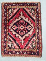 Full view of the rectangular hand knotted wool rug with tribal geometric and floral patterns in red, cream, and dark blue.