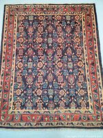 Full view of the rectangular Persian rug displaying intricate floral and geometric patterns with navy blue background and large border.