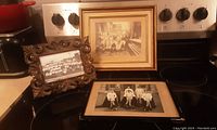Three framed black and white photos displayed on a stove top, showing two factory group photos and one sports team photo.