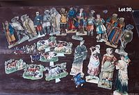 Photo of a large variety of Victorian paper cut outs on wood surface, including men, women, soldiers, and animals.