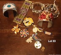 Overview photo showing all jewelry including bracelets, pins, and brooches arranged on wooden surface.