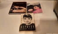 Three books on a flat surface: one hardcover and two softcover. The hardcover is the Courtney Love first edition, two softcover are Audrey Hepburn biographies.