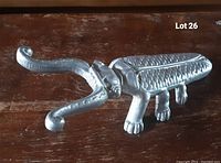 Side view of metal insect paperweight showing detailed wings, legs, and curled antennae on a wooden surface.