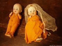 Photo showing full view of both Nippon dolls, bride and groom in yellow-orange crepe paper clothing with visible wear, bride wearing veil.